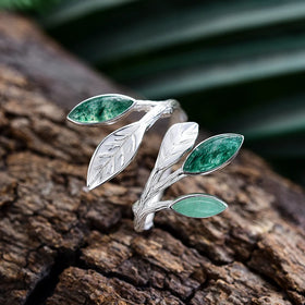 Silver leaf-shaped ring with green gemstones on a textured surface