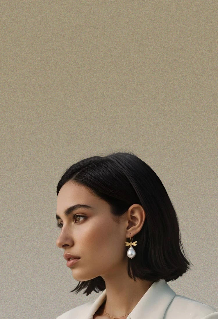 Woman wearing pearls and dragonflies earrings against a beige background