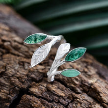 Silver leaf-shaped ring with green gemstones on a textured surface