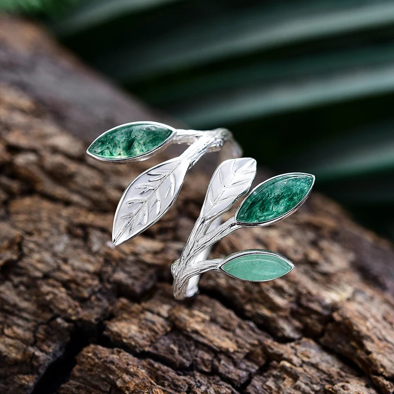 Silver leaf-shaped ring with green gemstones on a textured surface